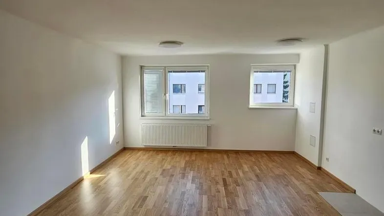 Helles, leeres Zimmer mit Parkettboden und zwei Fenstern, bereit zur individuellen Gestaltung.