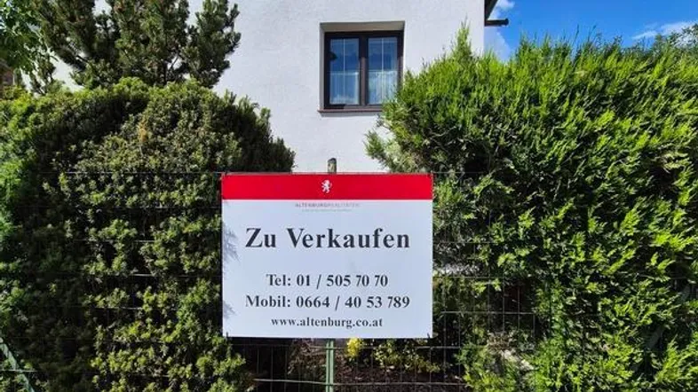 Vorderansicht des Hauses mit einem 'Zu Verkaufen'-Schild im Vorgarten.