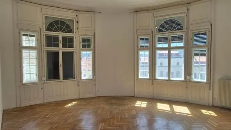 Helles, geräumiges Zimmer mit Fischgrätparkett und hohen Bogenfenstern, ideal als Wohnbereich.