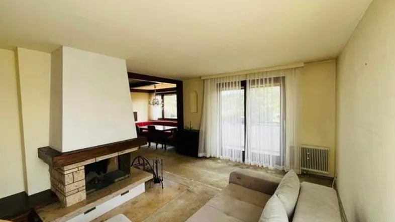 Geräumiger Wohnbereich mit Kamin, Sofa und Blick in den Essbereich, mit großen Fenstern.