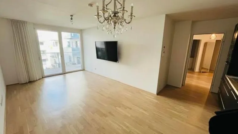 Helles Wohnzimmer mit Parkettboden, Kronleuchter und Zugang zu einem Balkon.