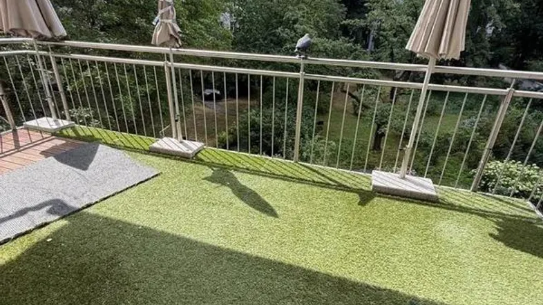 Balkon mit Kunstrasen und Blick ins Grüne, ausgestattet mit Sonnenschirmen.