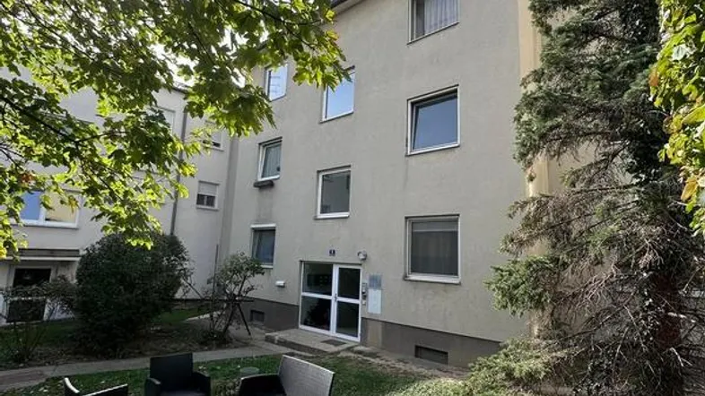 Außenansicht eines Mehrfamilienhauses mit gepflegtem Garten und gemütlicher Sitzgelegenheit im Freien.