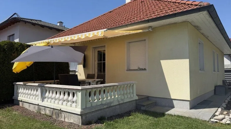 Gemütliche Terrasse mit Gartenmöbeln, Sonnenschirm und Markise, umgeben von einem gepflegten Rasen.