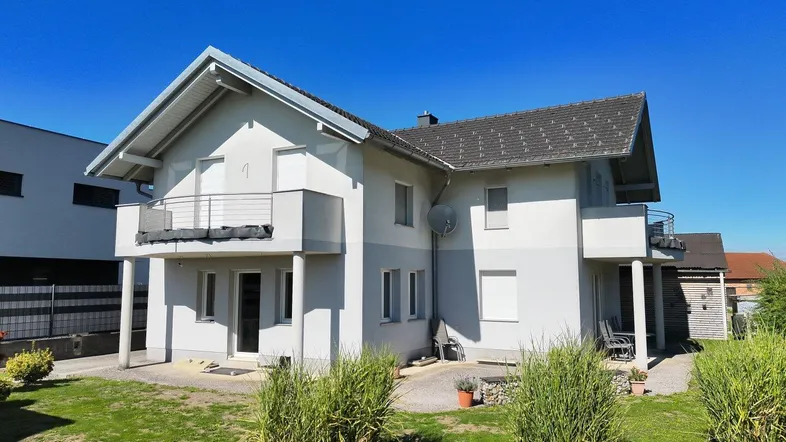 Modernes Einfamilienhaus mit Balkonen und gepflegtem Vorgarten unter blauem Himmel.
