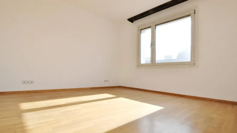 Helles Zimmer mit Parkettboden und großem Fenster, durch das viel Sonnenlicht einfällt.