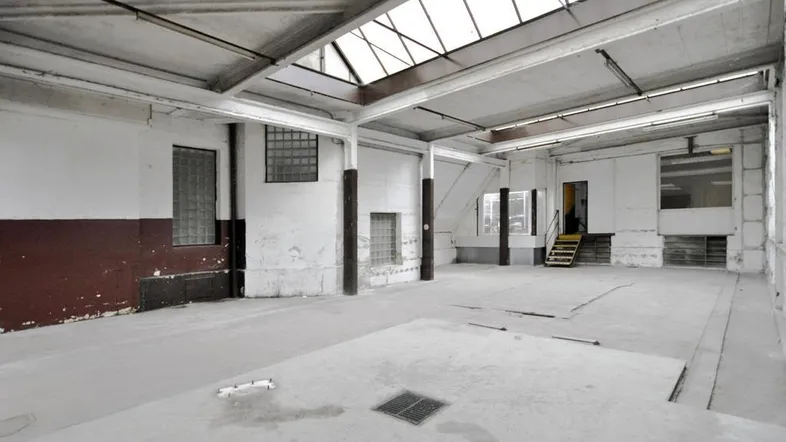 Großer, leerer Industrieraum mit hohen Decken, Oberlichtern und Betonboden, der eine umfassende Renovierung benötigt.