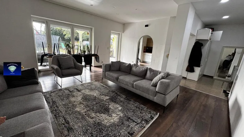 Geräumiges Wohnzimmer mit dunklem Holzboden, bequemen Sofas und Zugang zum Gartenbereich.