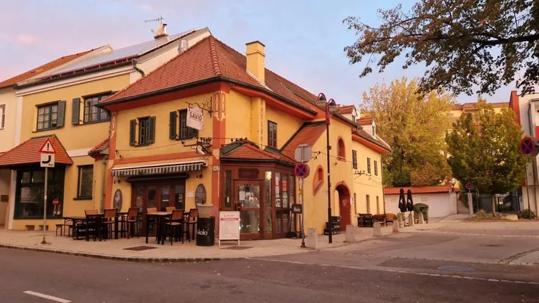 Charmantes gelbes Gebäude mit rotem Ziegeldach und Außenterrasse an einer städtischen Straße.