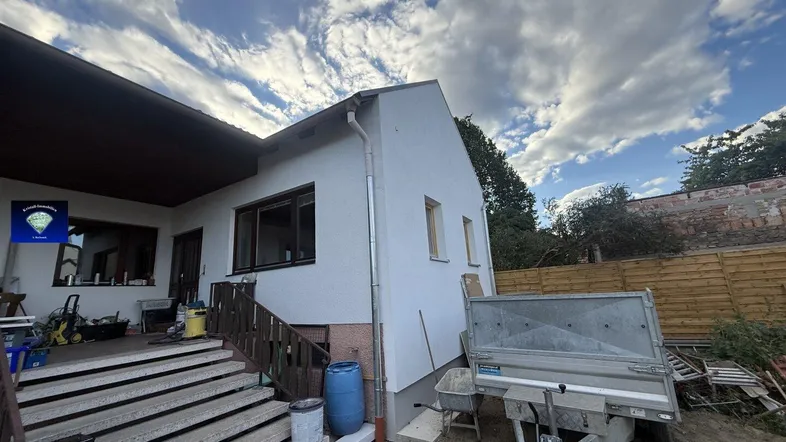 Außenansicht des Hauses mit Treppe und Baustellenbereich unter einem bewölkten Himmel.