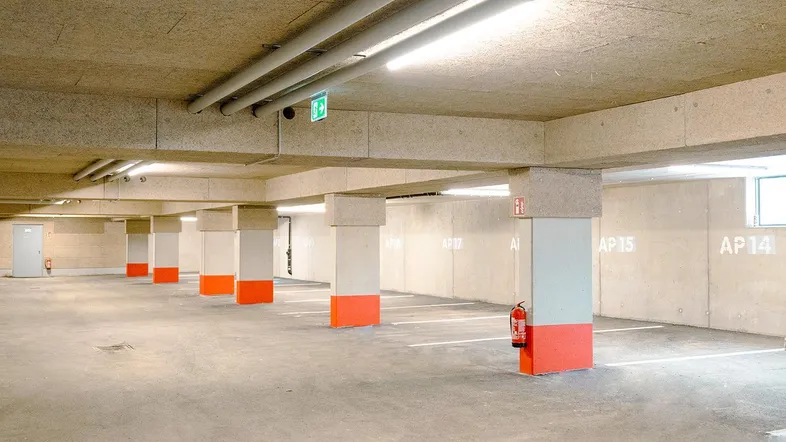 Helle Tiefgarage mit Betonwänden, orangefarbenen Säulen und effizienter Deckenbeleuchtung.