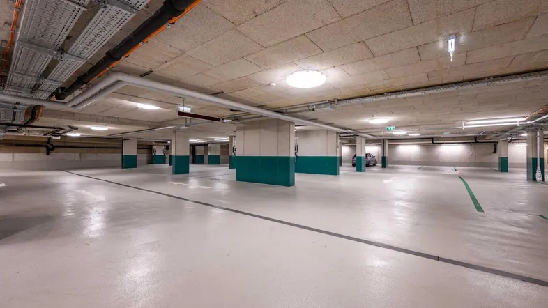 Helle und saubere Tiefgarage mit Betonboden und sichtbaren Installationen an der Decke.