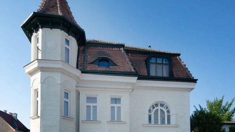 Historische Villa mit markantem Turm und traditionellem Ziegeldach unter blauem Himmel.