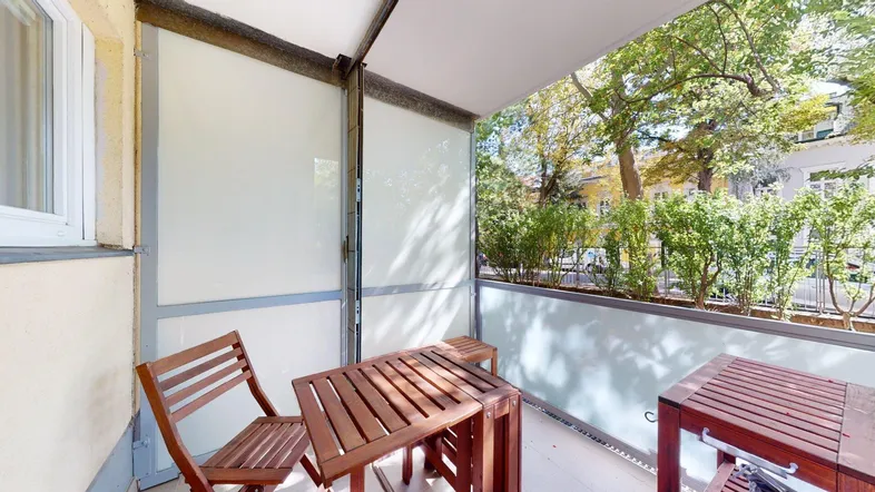 Gemütlicher Balkon mit Holztisch und Stühlen, umgeben von grünen Bäumen und Sträuchern.
