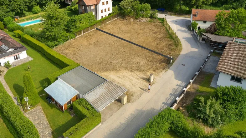 Luftaufnahme eines unbebauten Grundstücks in ländlicher Umgebung mit angrenzenden Wohnhäusern und viel Grün.