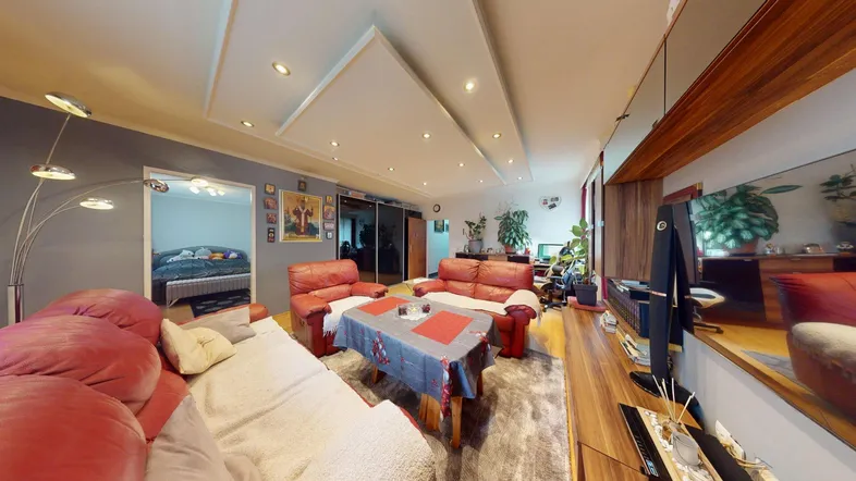 Geräumiges Wohnzimmer mit roten Ledersofas, Parkettboden und indirekter Deckenbeleuchtung.