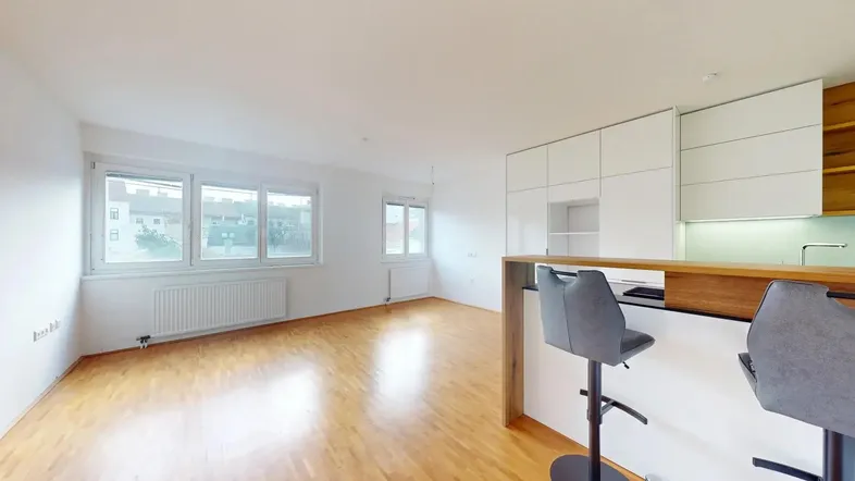 Heller offener Wohn- und Essbereich mit Holzboden, großen Fenstern und integrierter Küchenzeile mit Bar.