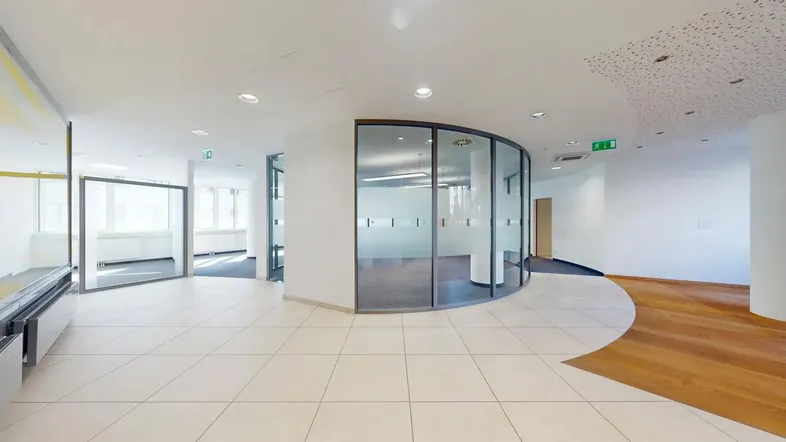 Heller Bürobereich mit modernen Glaswänden, Fliesenboden und Holzakzenten, ideal für flexible Arbeitsplatzgestaltung.
