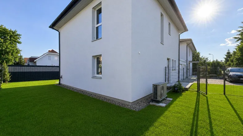 Moderne Hausfassade mit gepflegtem Rasen und Klimaanlage im Freien unter strahlendem Sonnenschein.