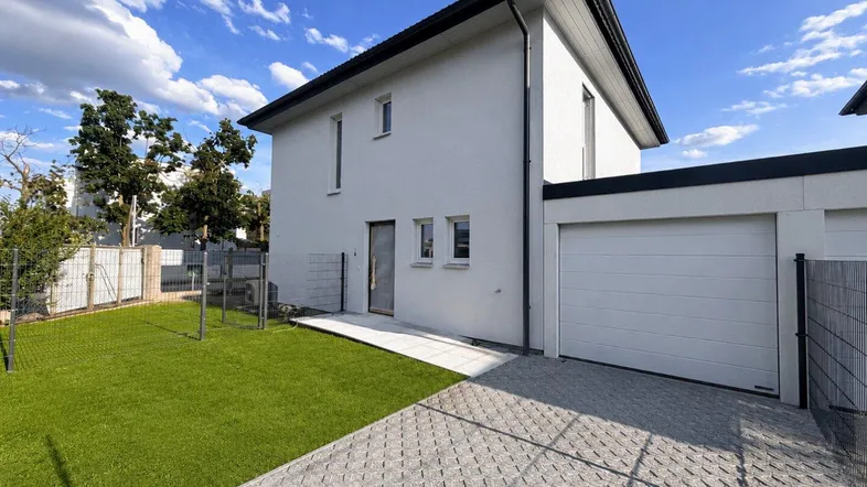 Modernes Einfamilienhaus mit weißer Fassade, Garage und gepflegtem Vorgarten unter blauem Himmel.