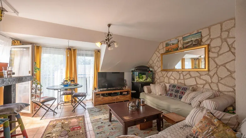 Gemütliches Wohnzimmer mit Steinwand, bequemen Sofas, Fernseher und Zugang zu einem kleinen Balkon.