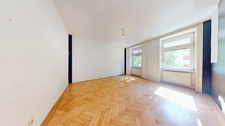 Helles Zimmer mit Fischgrätparkettboden und zwei Fenstern, bereit zur individuellen Gestaltung.