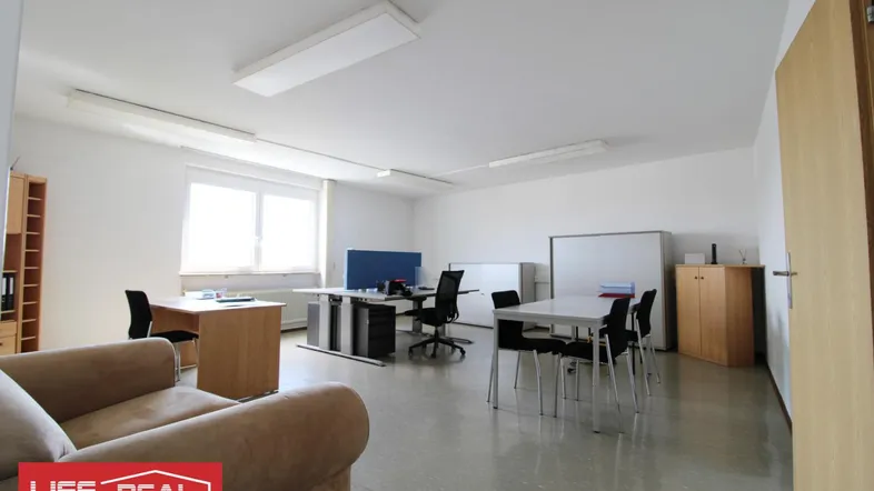 Geräumiges Büro mit mehreren Arbeitsplätzen, einem Besprechungstisch und viel Tageslicht durch große Fenster.