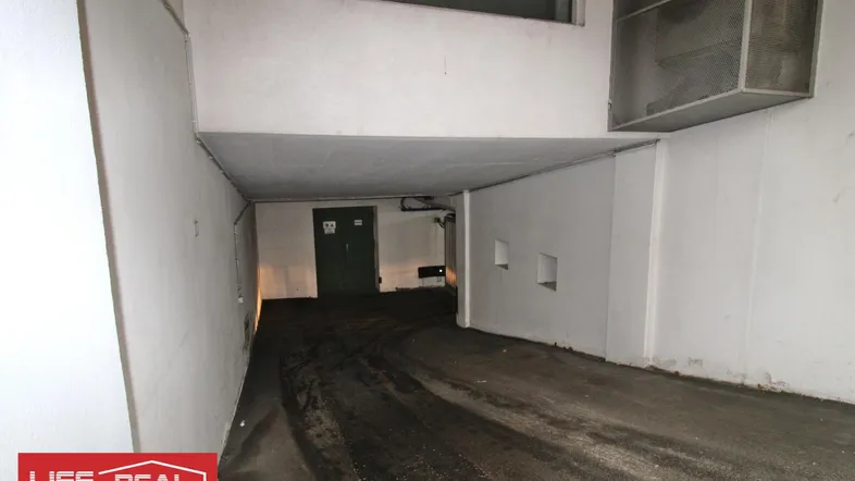 Einfahrt zu einer Tiefgarage mit dunklem Boden und weiß gestrichenen Wänden.