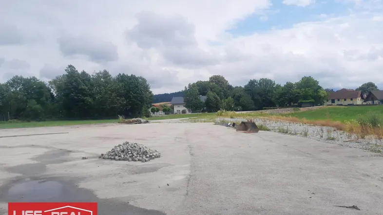 Ungenutztes Grundstück mit Betonfläche und Blick auf die umliegende Landschaft und Häuser unter bewölktem Himmel.