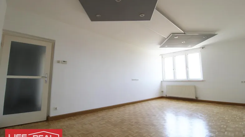 Helles, leeres Zimmer mit Parkettboden und modernen Deckenelementen, bereit zur individuellen Gestaltung.