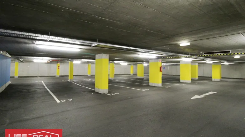 Geräumige Tiefgarage mit zahlreichen Stellplätzen, gelb markierten Säulen und Betonwänden.