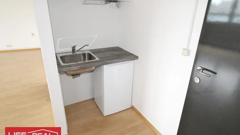 Kleine Küchenzeile mit Spüle, Arbeitsplatte und Kühlschrank, ideal für ein Apartment oder Büro.