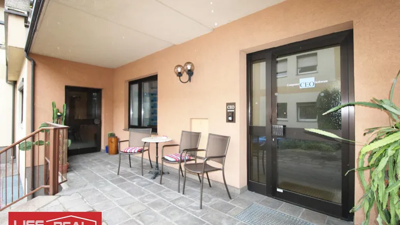 Überdachte Terrasse mit Sitzgelegenheiten und Zugang zum Gebäude, ideal für Pausen im Freien.