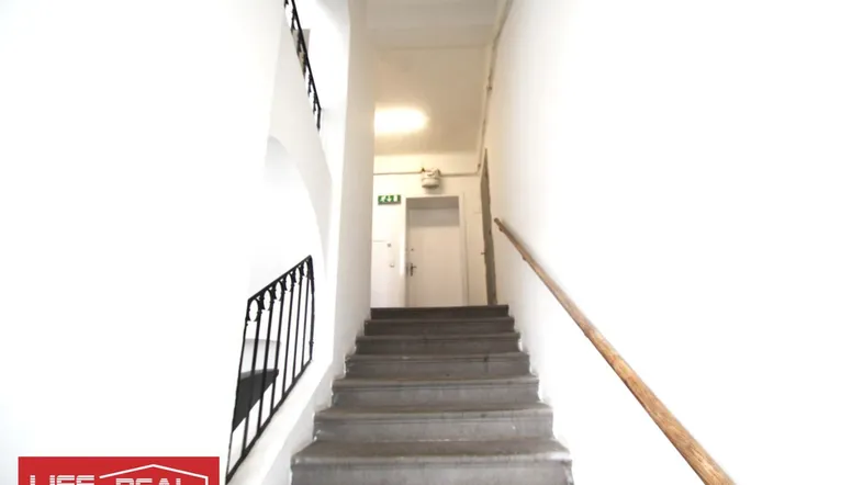 Helles Treppenhaus mit Steinstufen, weißen Wänden und einem Holzhandlauf, der nach oben führt.