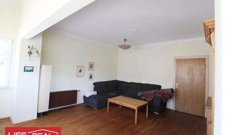 Gemütliches Wohnzimmer mit dunklem Ecksofa, Holztisch und Parkettboden, ideal zum Entspannen.
