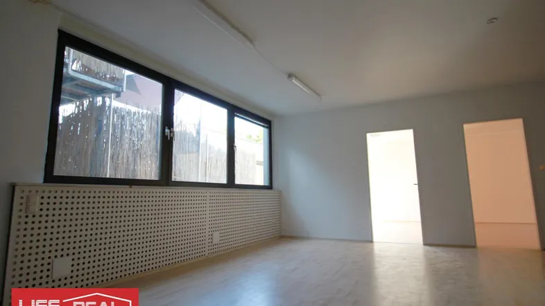 Heller Büroraum mit großen Fenstern, Heizungsverkleidung und hellem Laminatboden.
