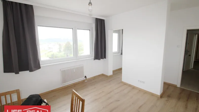 Helles Zimmer mit Laminatboden, großen Fenstern und Blick ins Grüne.
