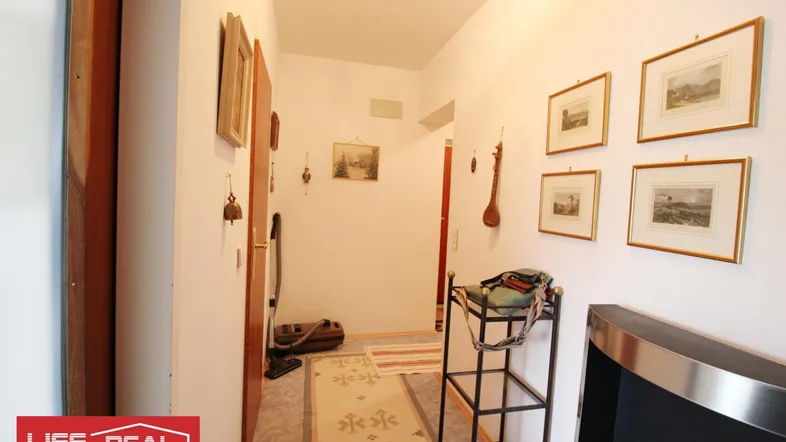 Heller Flur mit weiß gestrichenen Wänden, Teppichläufer und gerahmten Bildern an der Wand.