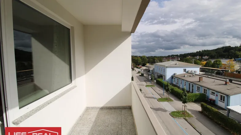 Balkon mit Fliesenboden und Blick auf die umliegende Bebauung und Landschaft unter bewölktem Himmel.