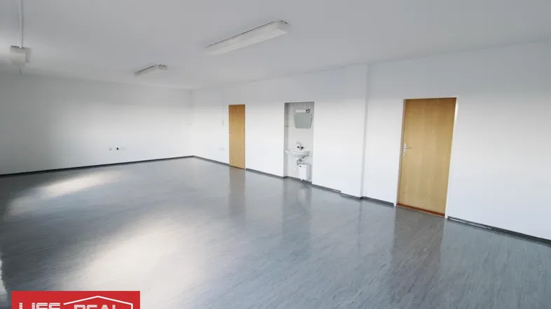 Geräumiger, leerer Raum mit grauem Vinylboden, weißen Wänden und zwei Holztüren, ideal für Büro oder Gewerbe.