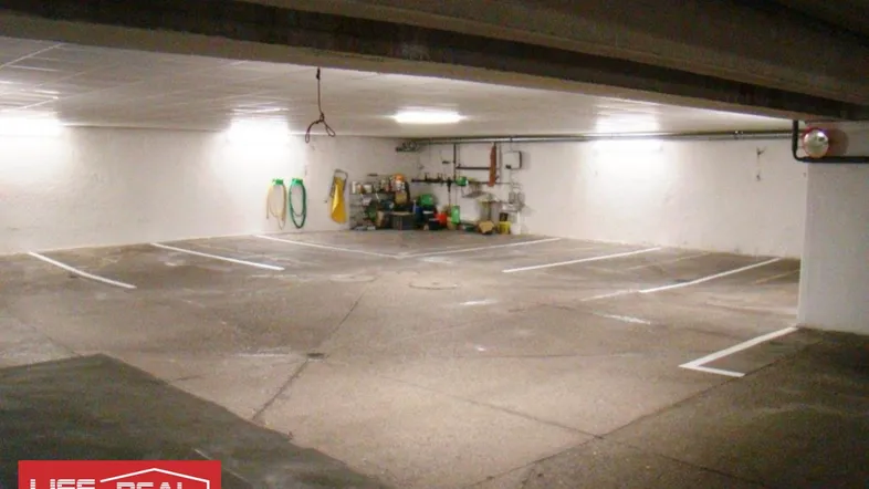 Leere Tiefgarage mit markierten Stellplätzen und Beleuchtung an den Wänden.
