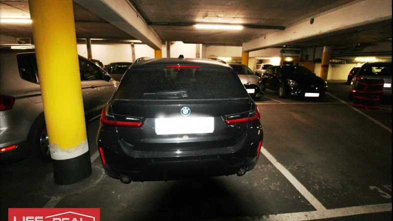 Tiefgarage mit geparktem Fahrzeug und gelbem Stützpfeiler in dunkler Umgebung.