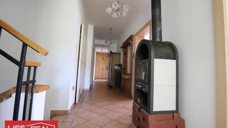 Heller Flur mit rustikalem Kaminofen, gefliestem Boden und Holztreppe, die in die obere Etage führt.