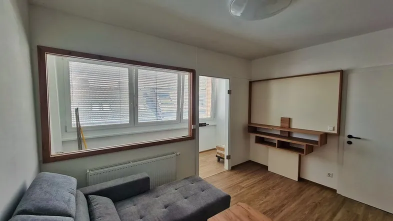 Helles Wohnzimmer mit modernem Sofa, Holzboden und einem Fenster mit Jalousien.