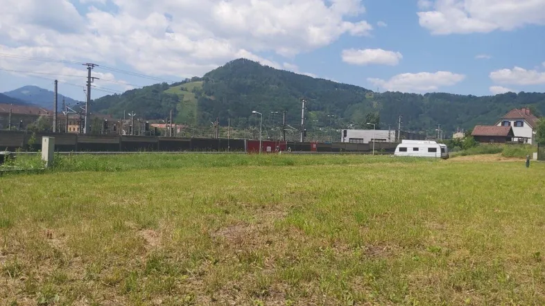 Weitläufiges grünes Grundstück mit Bergblick und angrenzender Bahnlinie unter blauem Himmel.