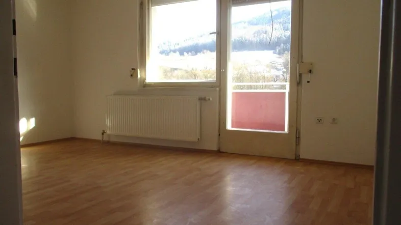 Helles Zimmer mit Parkettboden und Zugang zu einem Balkon, bietet einen weiten Blick auf die verschneite Landschaft.