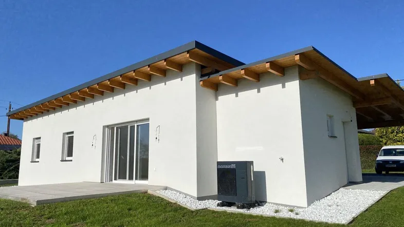 Modernes Einfamilienhaus mit weißer Fassade, Holzkonstruktion und Wärmepumpe auf grünem Rasen.