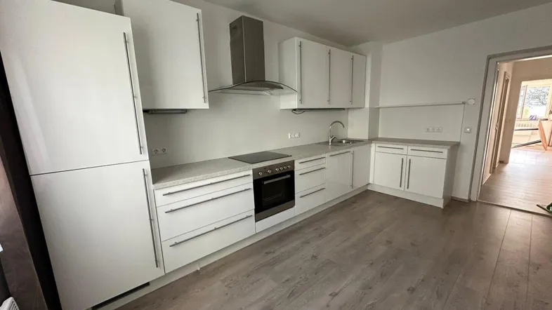 Moderne Küche mit weißen Schränken, integrierten Geräten und hellem Laminatboden.