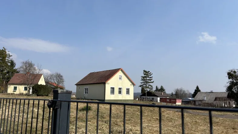 Ländliche Ansicht eines Hauses mit gelber Fassade und rotem Dach, umgeben von trockenem Grasland.