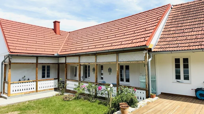 Traditionelles Haus mit überdachter Terrasse, Holzbalken und einem kleinen Vorgarten mit Rosen.